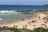 People on the sand and water with life savers under an umbrella on Mackenzies Bay beach