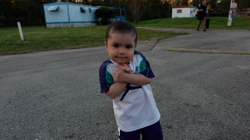 A little boy crosses his arms in front of his body in a trailer park