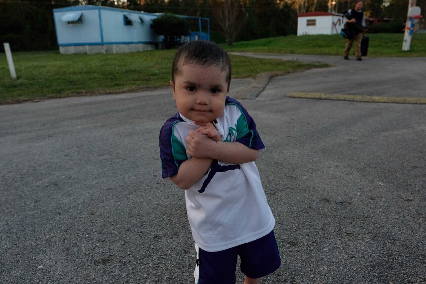 A little boy crosses his arms in front of his body in a trailer park