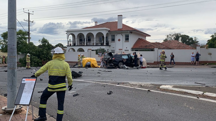 A firefighter can be seen at the site of a car crash. Debris is strewn across the road.