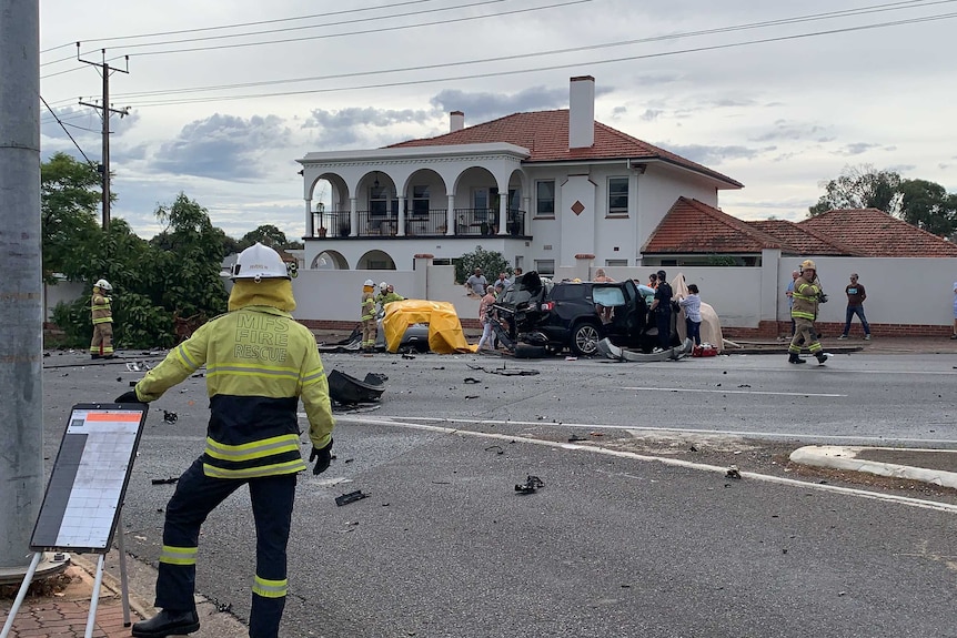 A firefighter can be seen at the site of a car crash. Debris is strewn across the road.