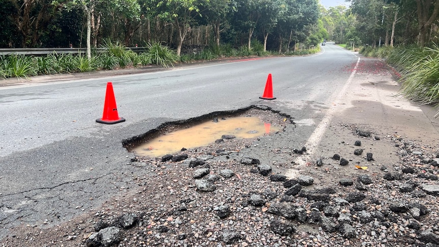 A big pothole with traffic cones placed around it.