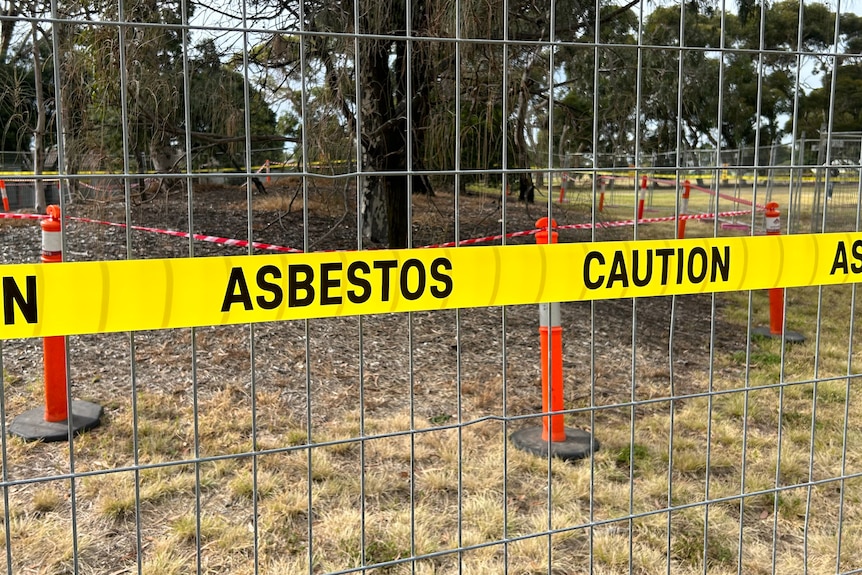 A yellow sign at a park says 'Asbestos: caution'.