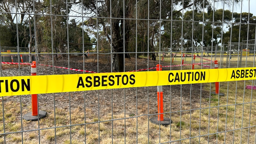 A yellow sign at a park says 'Asbestos: caution'.