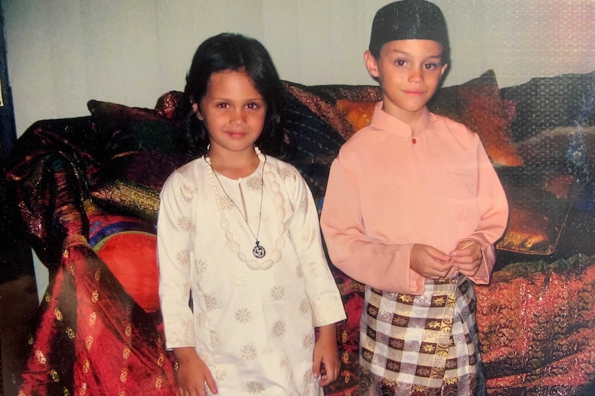 Amishah, left, stands next to her brother, right. They are both wearing traditional clothing and smile at the camera.