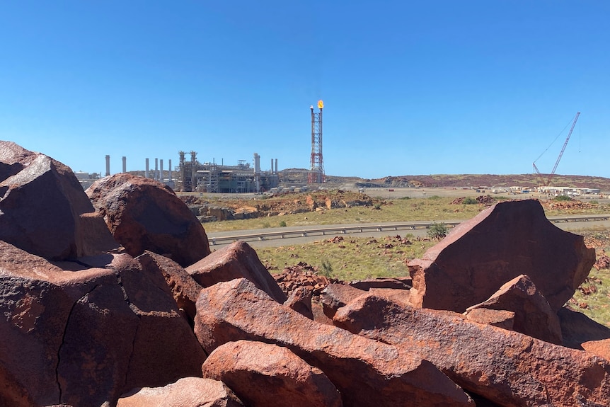 Rocas rojas en primer plano con una planta de gas en una zona rural en la parte posterior con una llamarada.