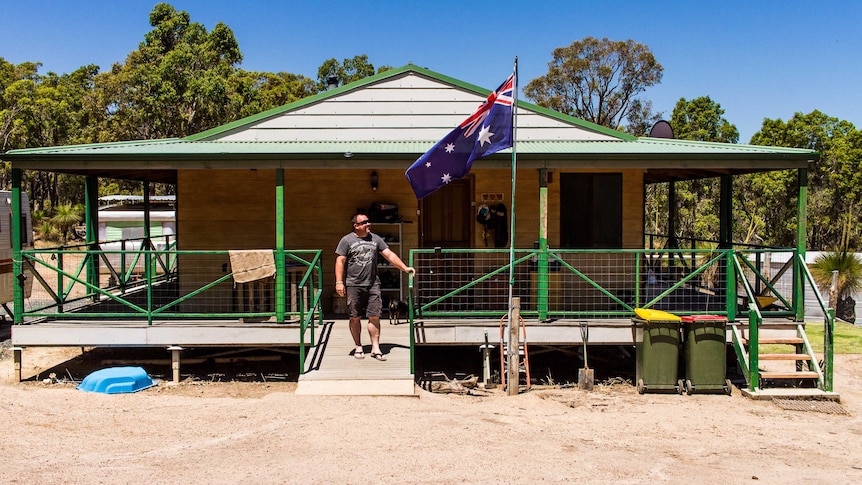 Brian Willcox stands on the verandah looking up at an Australian flag.