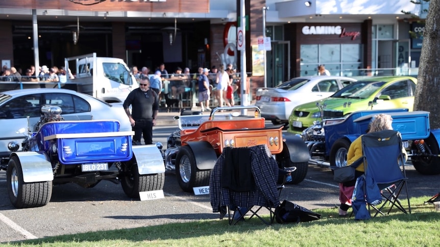 Three vintage buggies parked on the street with passers-by looking 