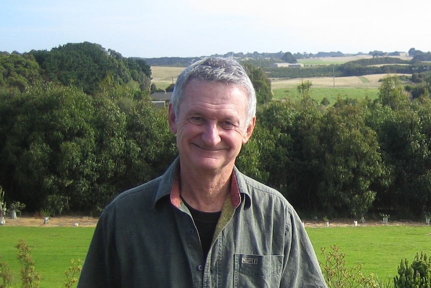 Children's author Paul Jennings smiles as he stands in front of bushland.