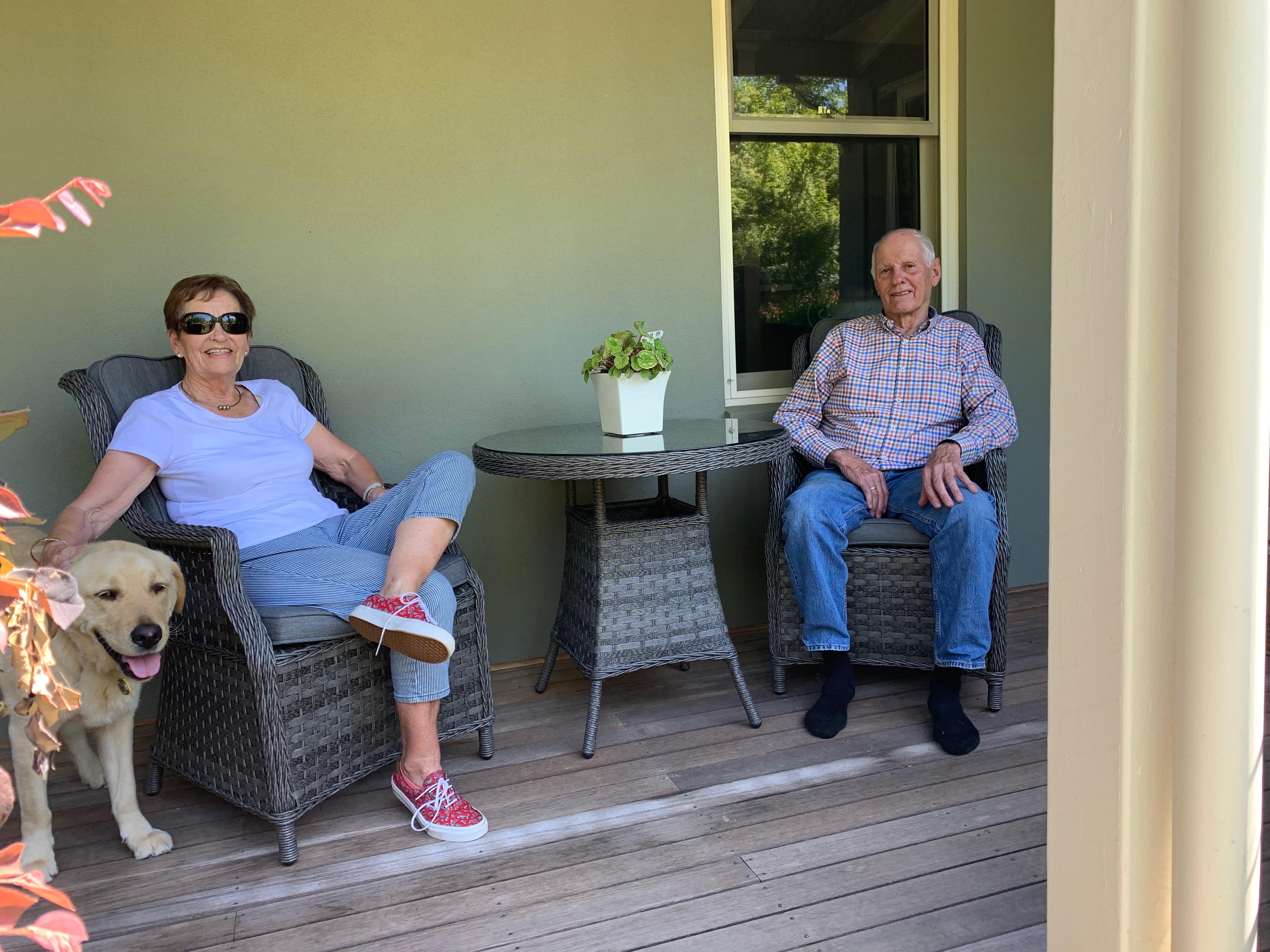 An man and a woman sit on a porch with a dog