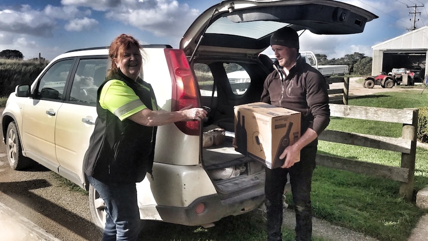 woman postie delivers box of wine to farmer at farm