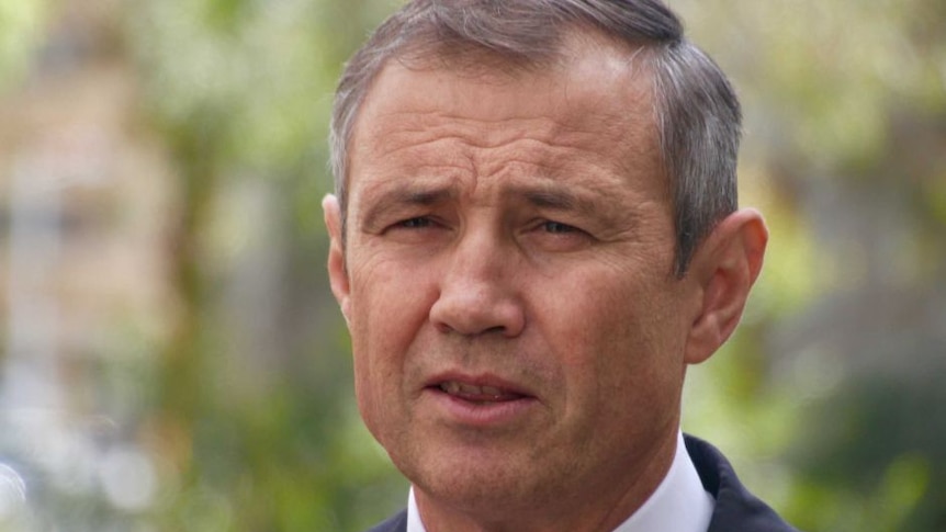 A head and shoulders shot of WA Health Minister Roger Cook talking outdoors wearing a suit and tie.