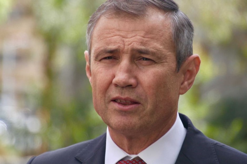 A head and shoulders shot of WA Health Minister Roger Cook talking outdoors wearing a suit and tie.