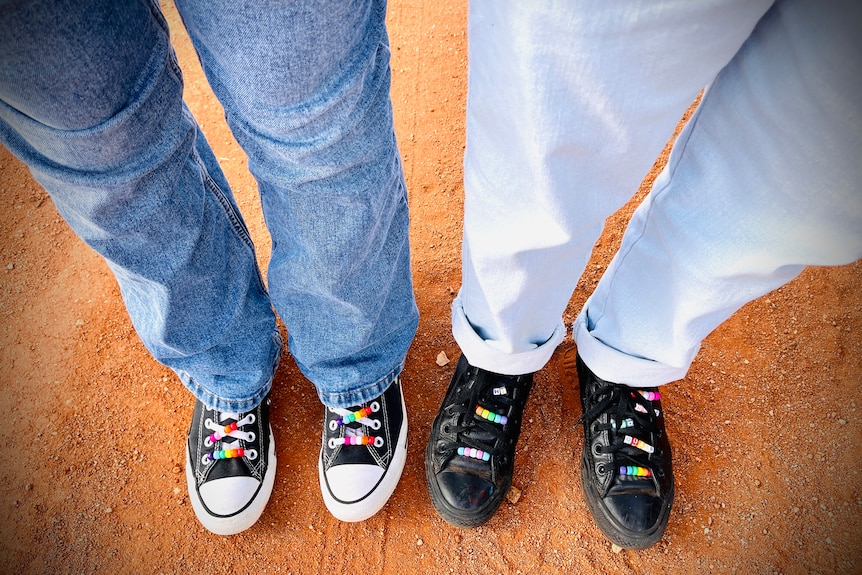 Two pairs of shoes standing next to each other, a black pair and a black and white one both rainbow beads in the shoe laces