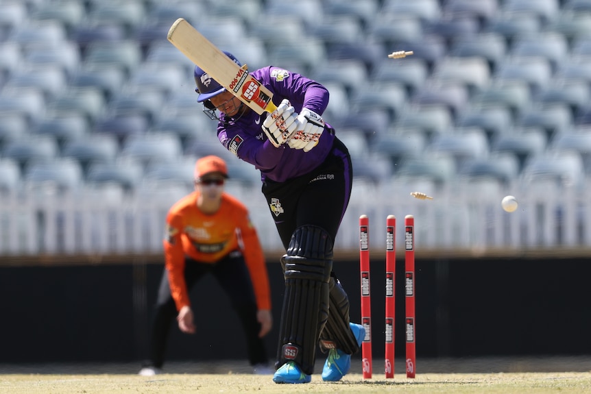 A batter leans forward as the bails fly in the air behind her in a WBBL game. 