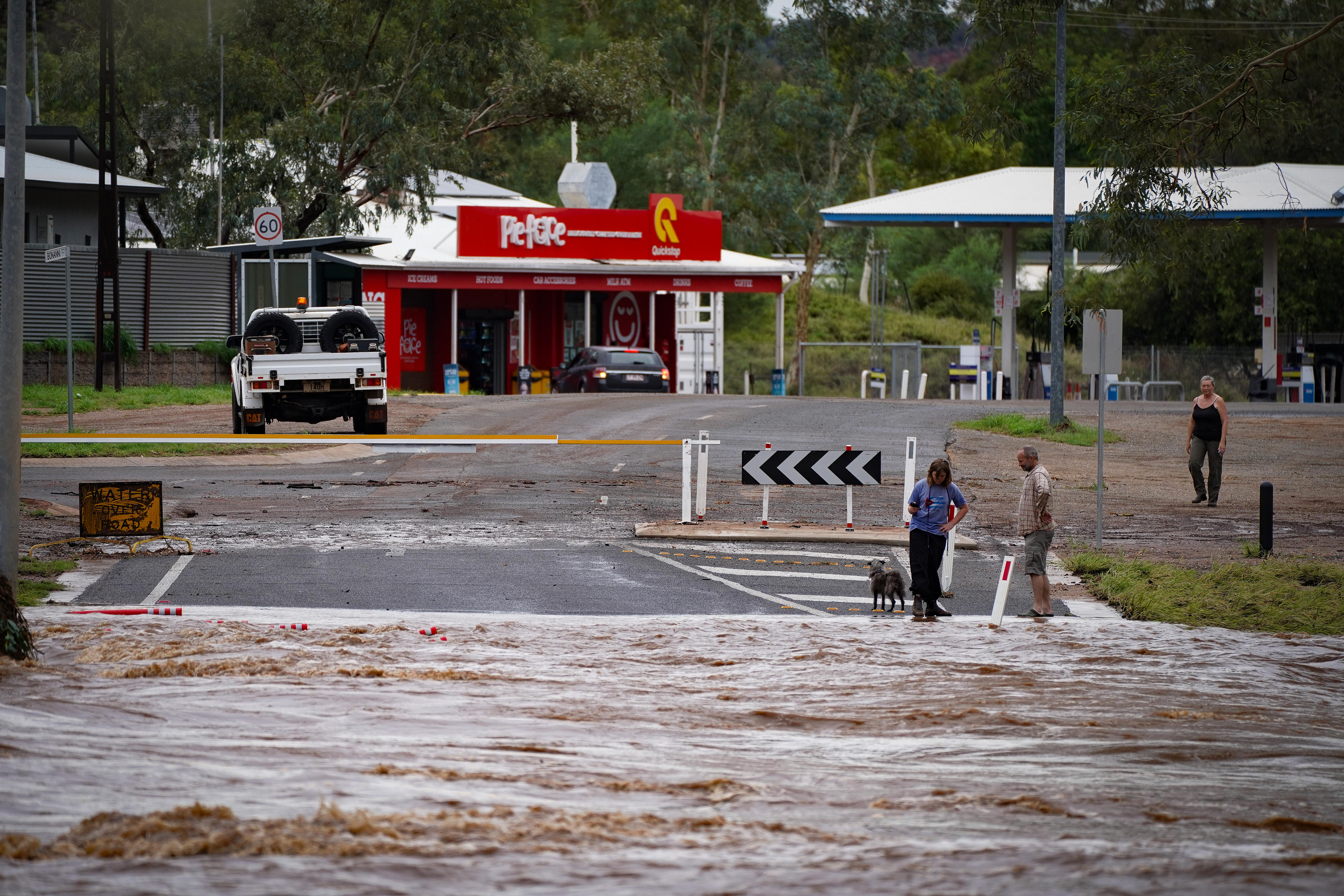 Uma estrada coberta de água, um carro de um lado e um posto de gasolina ao fundo 