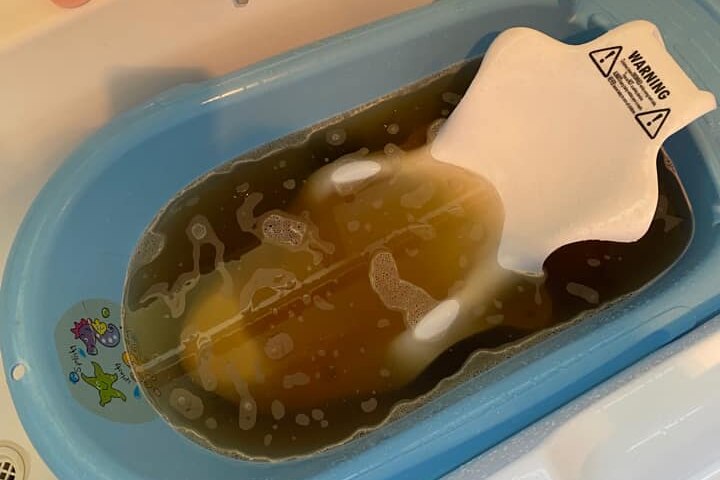 a baby bath sits in a household bath covered in brown water.