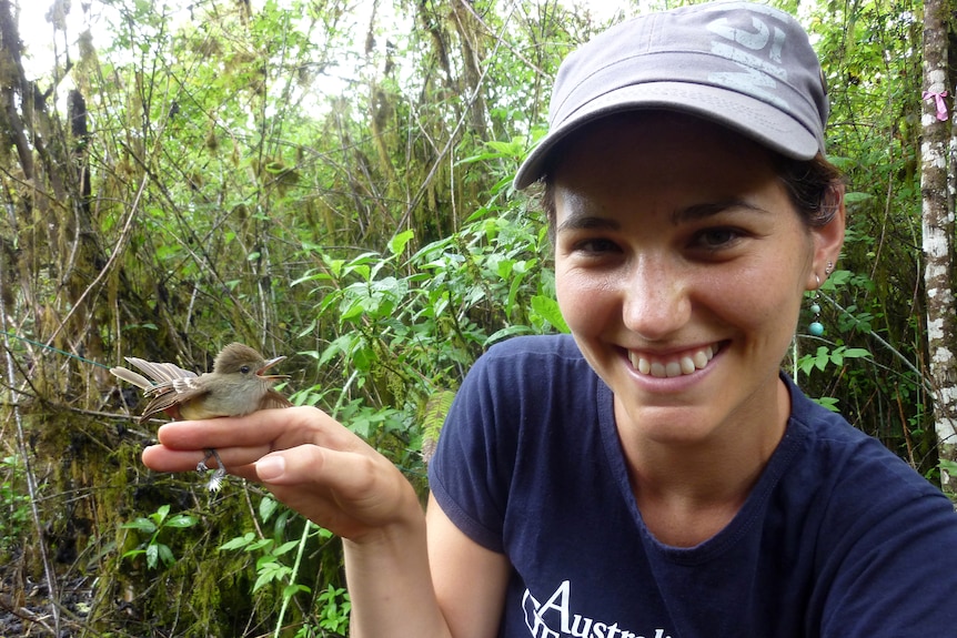 A woman in a forest smiles as a bird sits on her hand