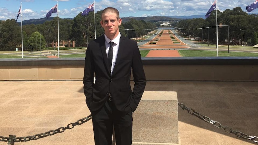 Liam Wolf standing on Federal Parliament forecourt with Anzac Parade and War Memorial behind him