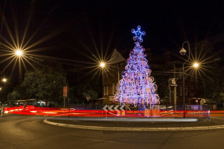 A large, mostly white Christmas tree made of bicycles with colourful wheels. Taken at night with street lights.