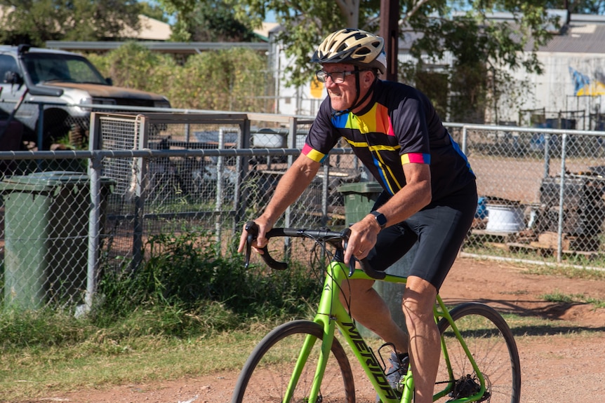 Dennis Dean, an older man, wears lycra on a green bike and rides through Yarralin. 