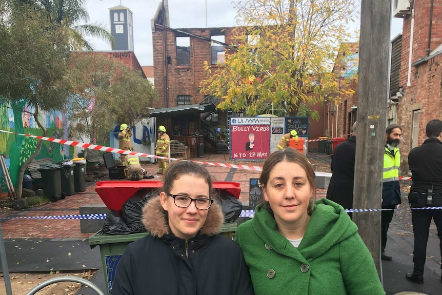 Two women stand on the street in front of the remains of the theatre.