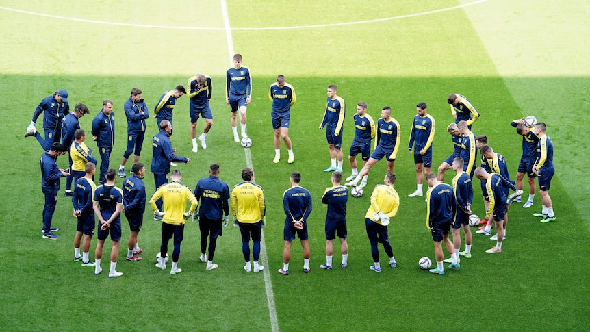 A coach talks to a group of players standing in a circle on a pitch in a football stadium in Wales.