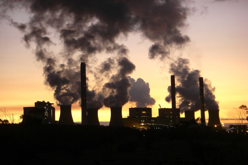 A power station in silhouette belching smoke into the low-lit sky.