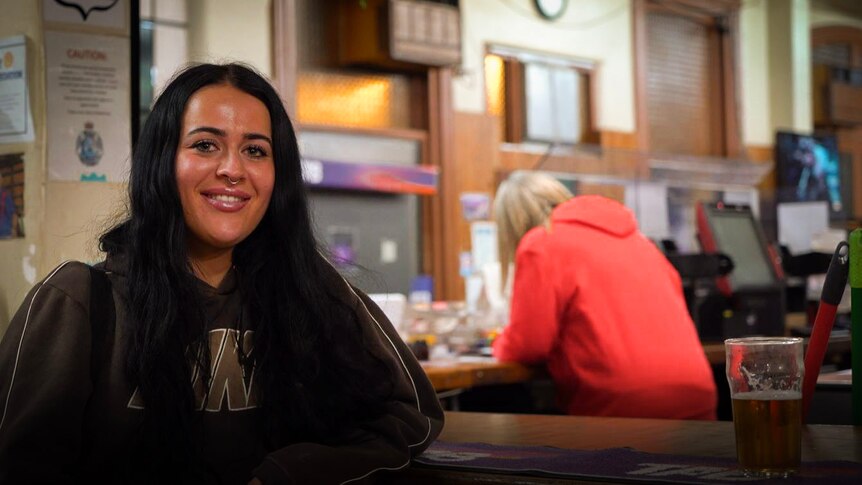 A woman in a hoodie sits at a bar smiling.