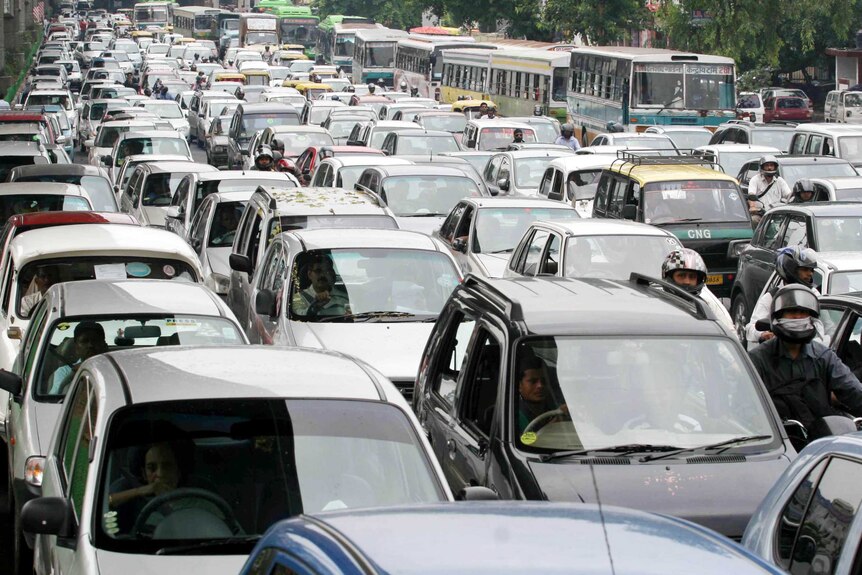Cars sit in tight traffic in the Indian capital Delhi. There are motorcycles between the cars and a row of buses to the side.