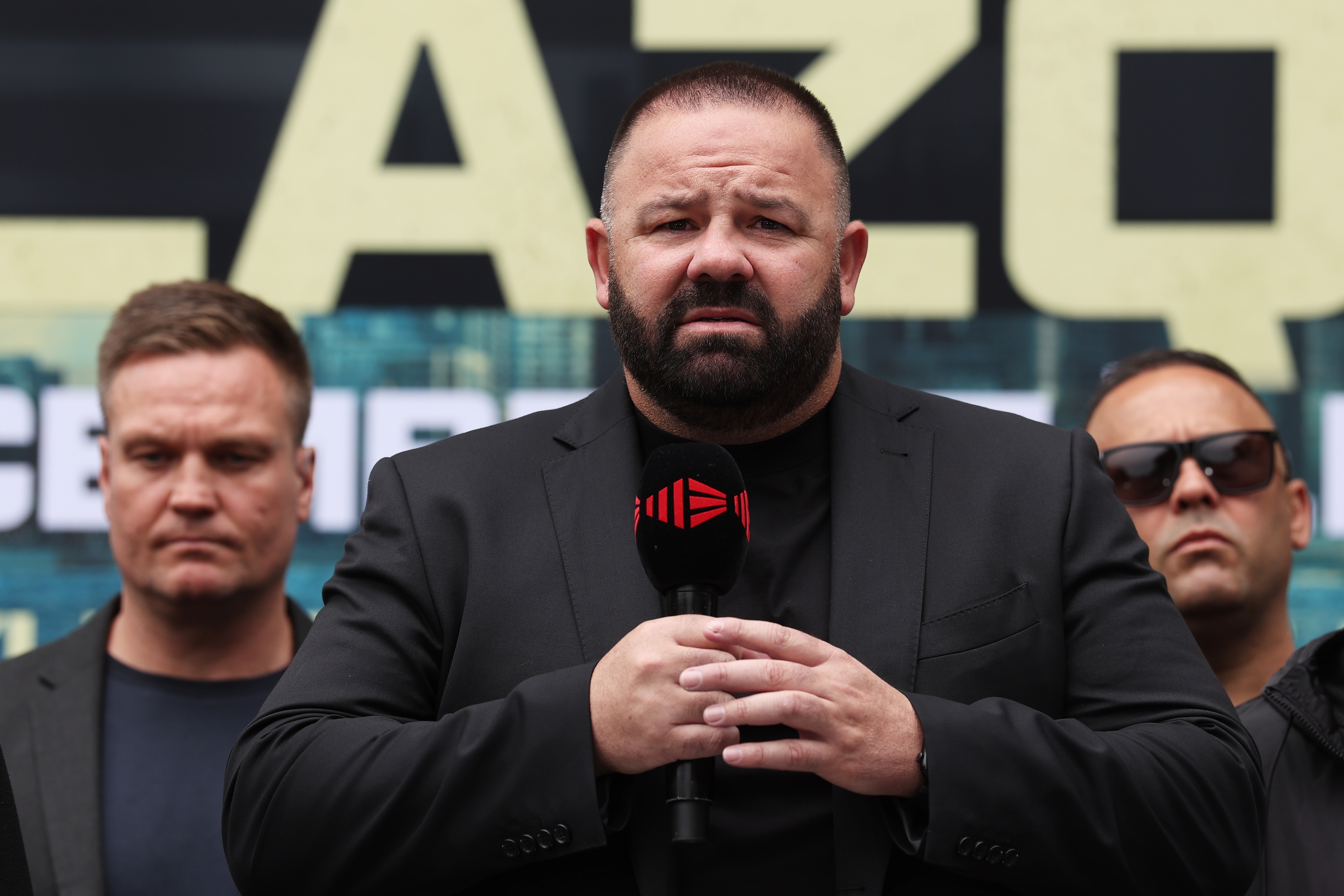 George Rose holds microphone with both hands and speaks
