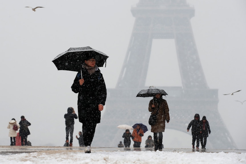 People use their umbrellas as they walk by the Eiffel Tower on a snowy day.