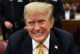 Trump smiles in a yellow tie and suit in a court