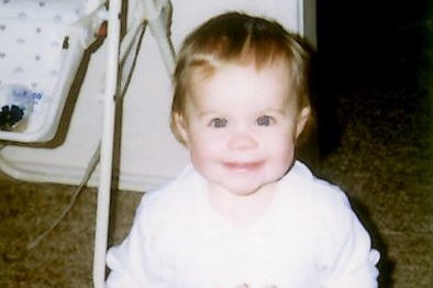 A toddler wearing a onesie smiles for the camera