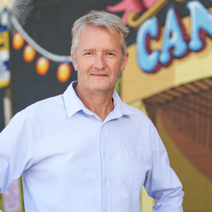 Ross Solly standing in front of a brightly painted carnival-style sign saying "Canberra".
