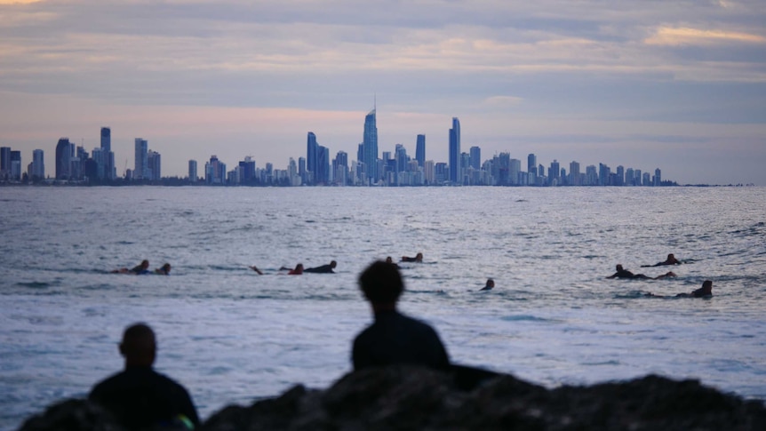 View across the water with surfers in the foreground paddling and the high-rises of Surfers Paradise in the background.