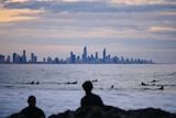 View across the water with surfers in the foreground paddling and the high-rises of Surfers Paradise in the background.