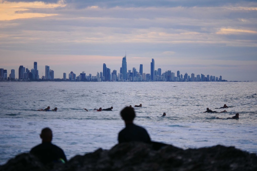 Views of the water with surfers in the foreground paddling and the high-rise buildings of Surfers Paradiose in the background