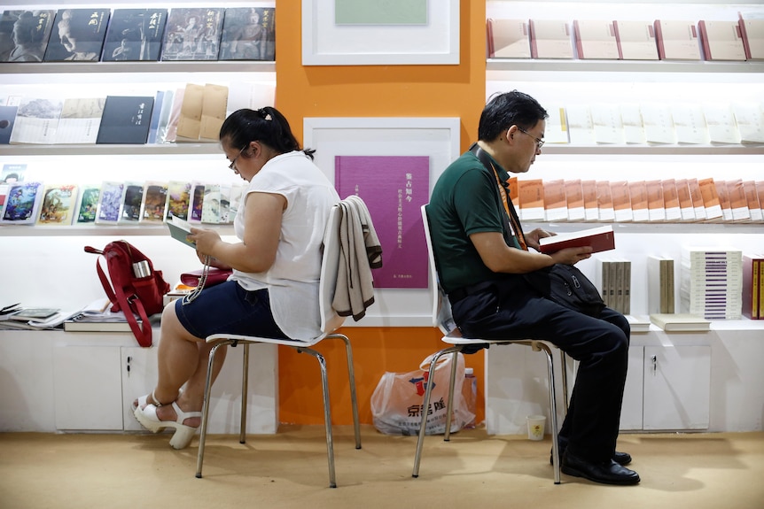 Dos personas se sientan en sillas y leen libros. 