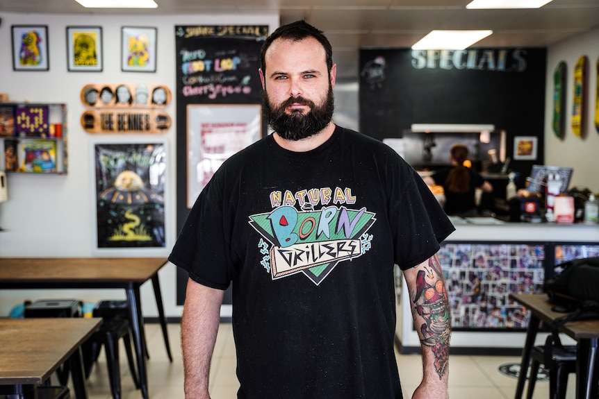 A man in a black t-shirt stands in a colorfully decorated restaurant space.