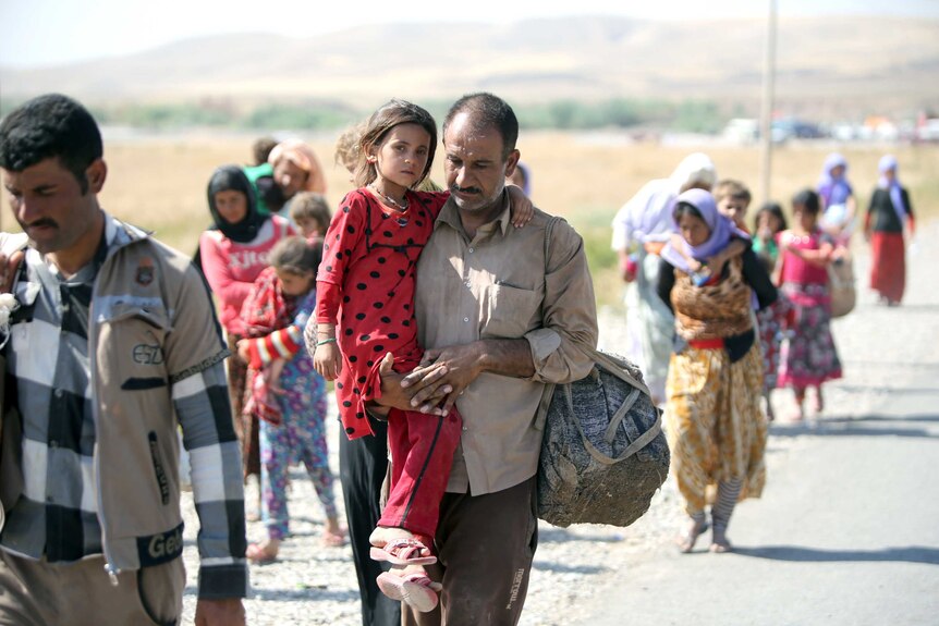 A displaced Iraqi man from the Yazidi community carries his daughter across the Iraqi-Syrian border.