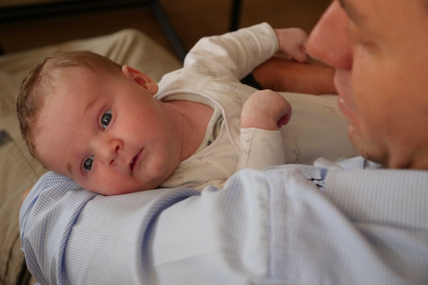 A father holding a three-week old baby in his arms.