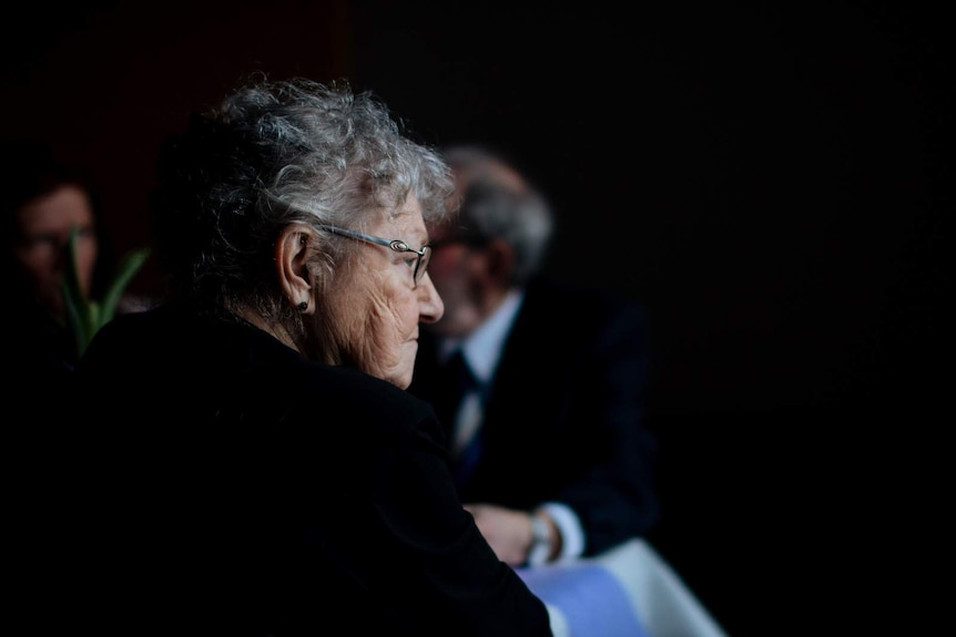 An older woman sits in a dark room.