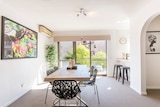 A large dining table is seen near the balcony of a brightly lit inner suburb apartment
