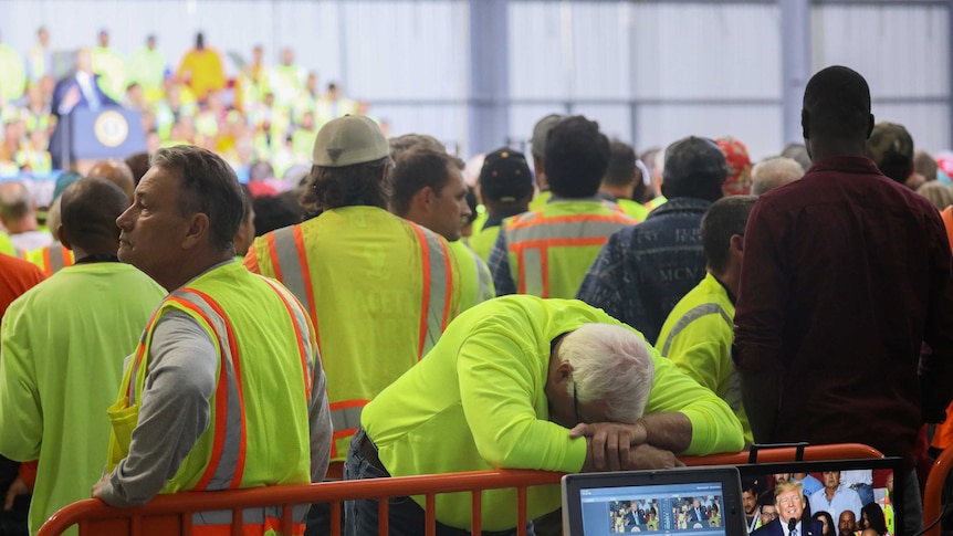 In a crowd of men in yellow vests, one slumps with his head on a fence