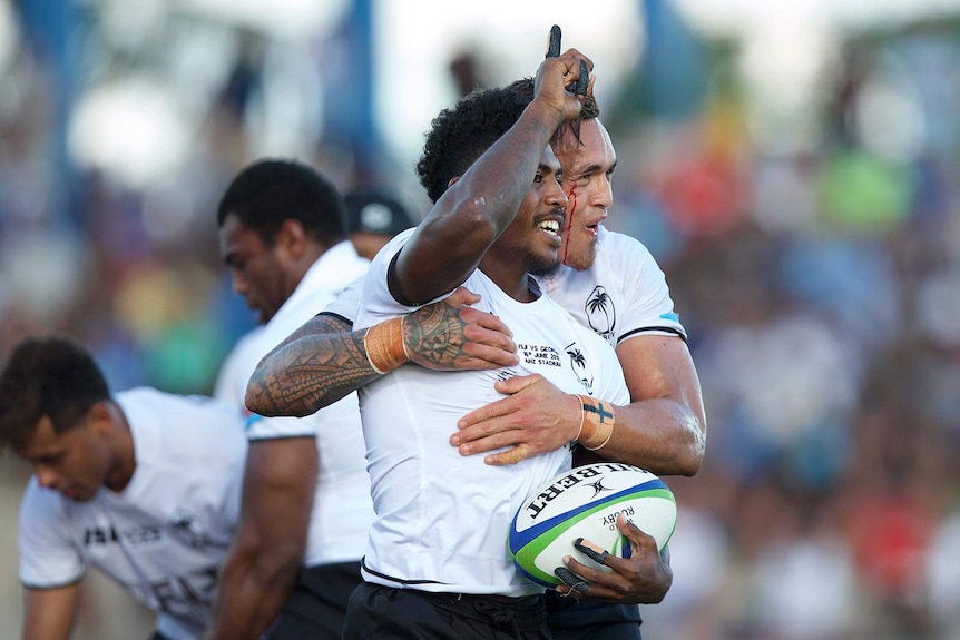 One Rugby player embraces another player who is pointing to the sky.