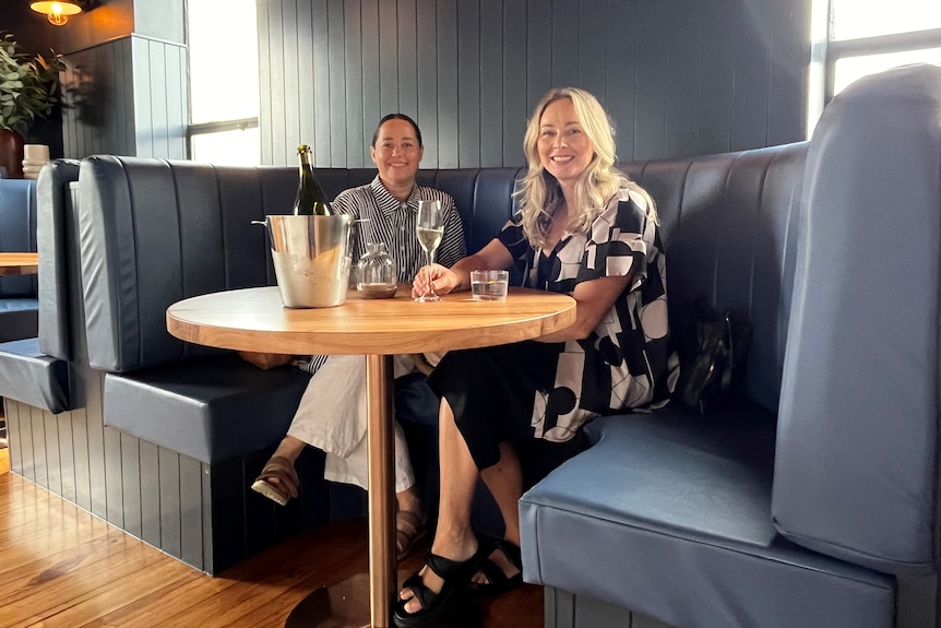 Dos mujeres en un stand azul en un restaurante con una botella de champán y copas