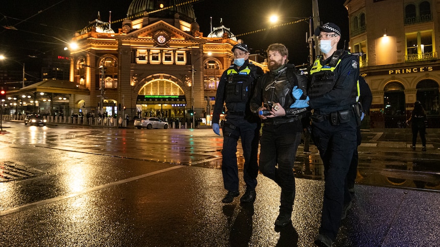 Two police officers lead away a man outside Flinders Street Station at night.