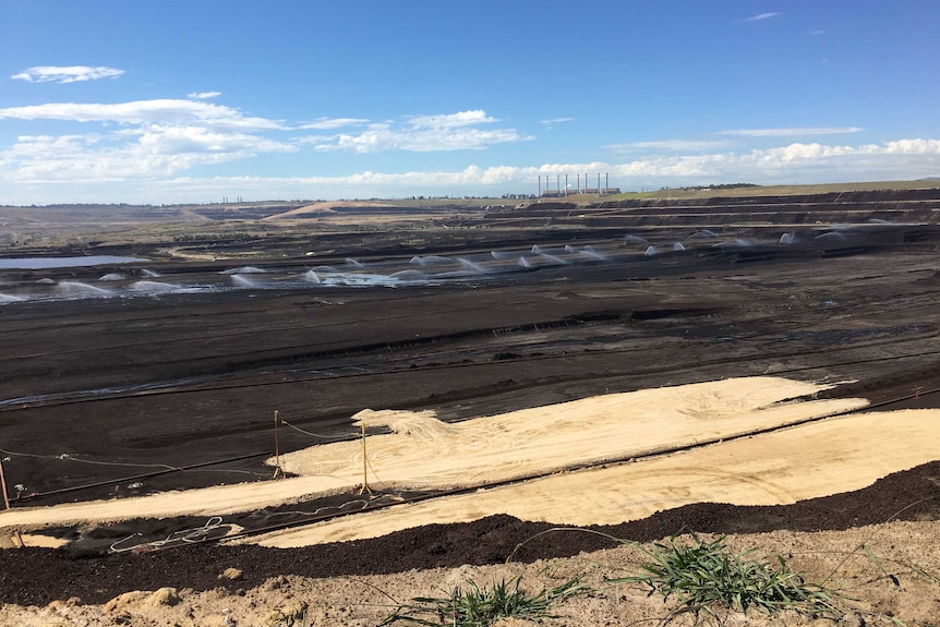 A giant open cut coal mine with a power station in the background