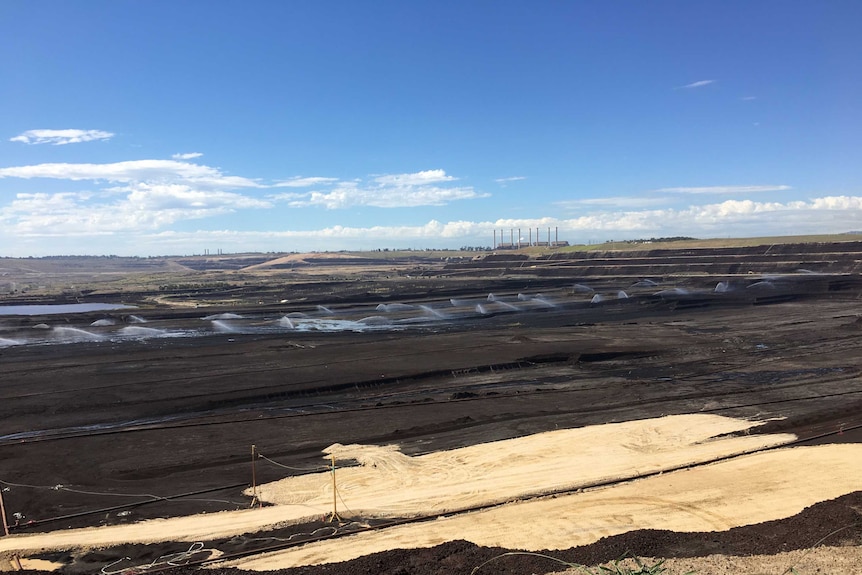 A giant open cut coal mine with a power station in the background